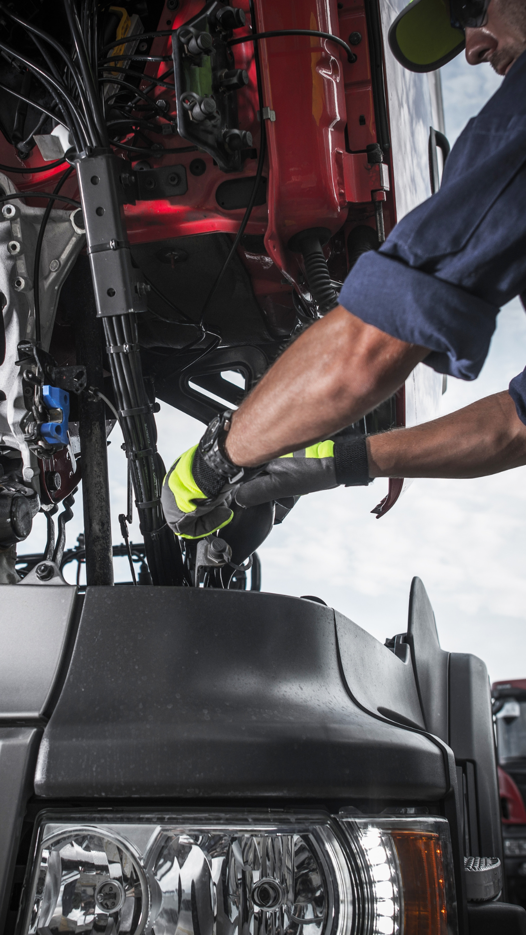 Se ven las manos de un mecánico con guantes grises amarillos, reparando un cable de un camión